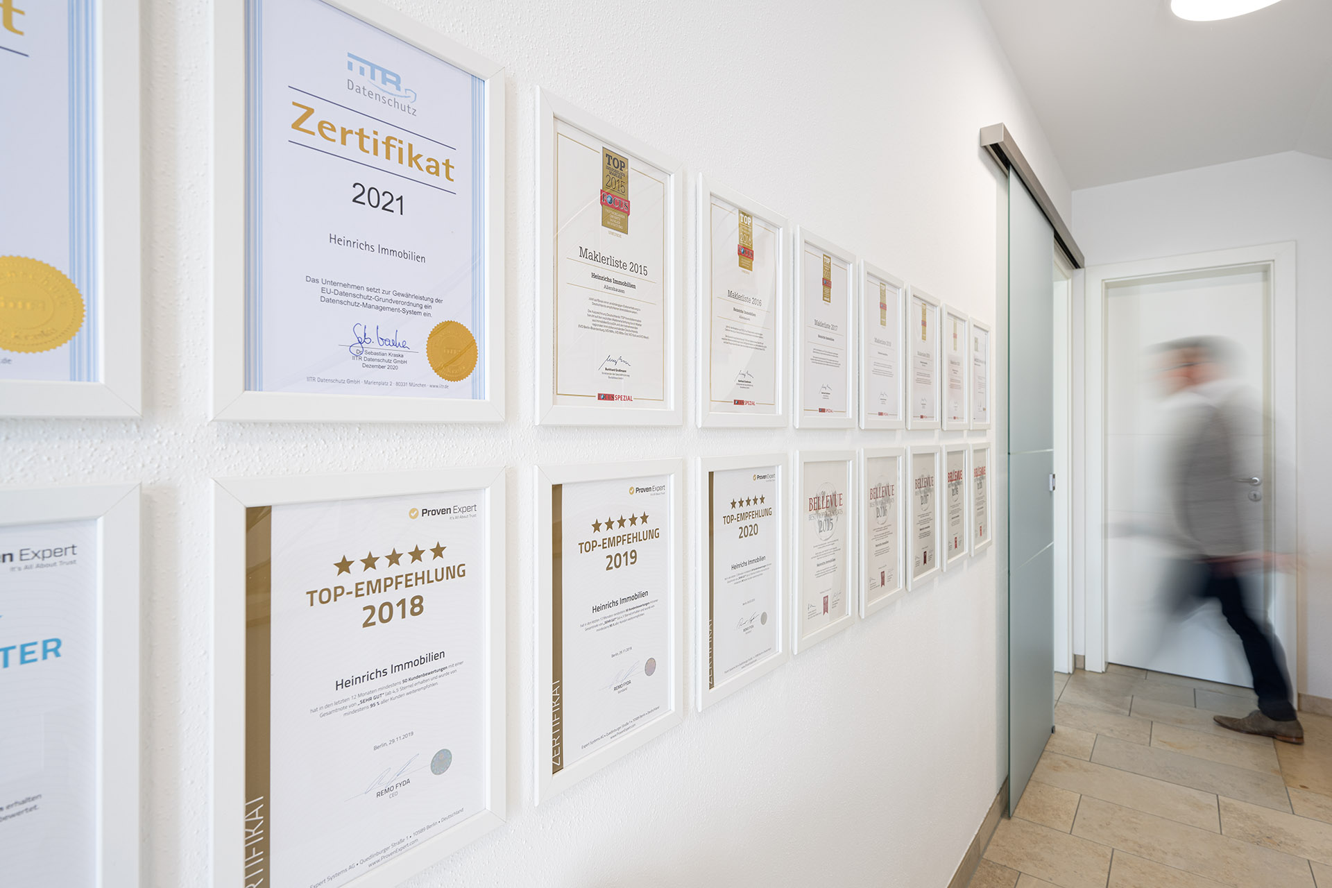 Wand mit gerahmten Auszeichnungen und Zertifikaten von Heinrichs Immobilien
